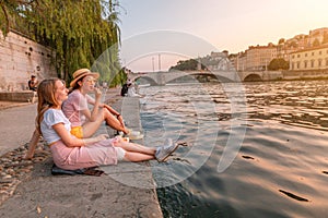 Happy caucasian and asian girls friends meeting great sunset on a river Saone in Lyon city. Travel and lifestyle in France