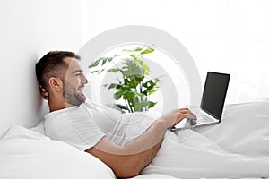 Happy caucasian attractive millennial male in white t-shirt woke up, surfing, searches and chatting and work on pc