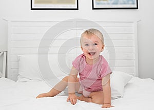 Happy caucasian baby girl about 1 year old having her two first milk teeth laughing sitting on bed.Adorable child