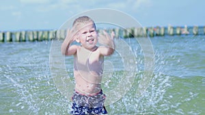 happy caucasian baby kid boy splashing playing in sea ocean water in sunny day.