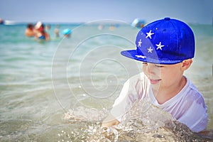 Happy caucasian boy is bathing in sea water on beach against are swimming people on horison. Summer vacation on sunny day