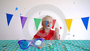 Happy caucasian boy with party noisemaker sit by birthday table. Gimbal motion