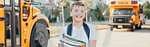 Happy Caucasian boy student with backpack and exercise books near a yellow bus on first September day. Education and back to