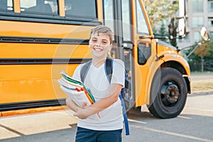 Happy Caucasian boy student with backpack and exrecise books near yellow bus on first September day. Education and back to school