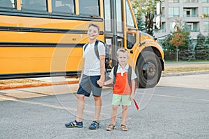 Happy Caucasian brothers students near yellow school bus. Smiling kids holding hands, going back to school in September. Education