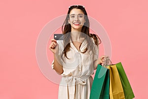 Happy caucasian brunette woman in stylish dress, carry shopping bags and credit card, paying everything with paypass