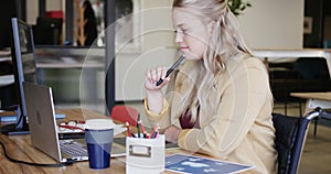 Happy caucasian casual businesswoman in wheelchair using laptop in office, in slow motion