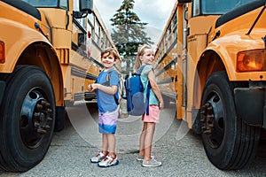 Happy Caucasian children boy and girl kids students standing by yellow school bus. Education and back to school in September.