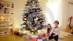 Happy Caucasian children and Yorkshire Terrier admiring Christmas gifts sitting at home in living room indoors talking