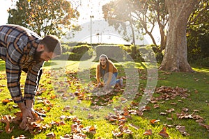 Happy caucasian couple collecting leaves in sunny autumn garden
