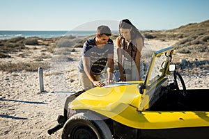 Happy caucasian couple reading roadmap on beach buggy by the sea