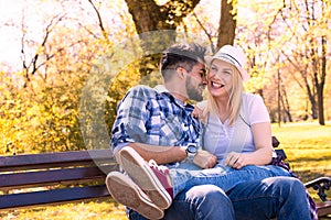 Happy caucasian couple sitting on a park bench, with the girl's legs on his lap