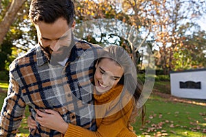 Happy caucasian couple walking in sunny autumn garden smiling and embracing