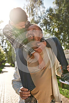 Happy caucasian dad carry on shoulders teenage son