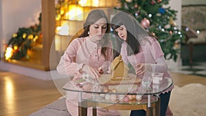 Happy Caucasian daughter and mother making ginger house in living room with New Year tree. Portrait of joyful positive