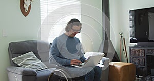 Happy caucasian disabled man in wheelchair using laptop in living room