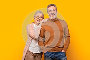 Happy Caucasian elderly couple embraces against yellow studio backdrop