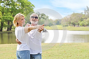 Happy caucasian elderly couple wearing white shirt, blue jean and sun glasses are dancing in the park during summer time with