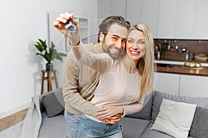 Happy caucasian family couple showing new house keys to camera while posing Indoors. Own home, real estate ownership and