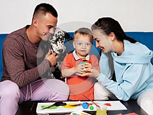 Happy Caucasian family with a Dalmatian dog are engaged in creative work at home and have fun. Mom, son and dad