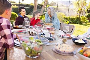 Happy caucasian family sitting at table and eating dinner together in sunny garden