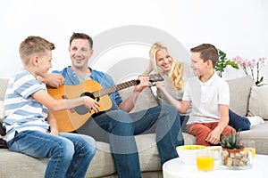 Happy caucasian family smiling, playing guitar and singing songs together at cosy modern home