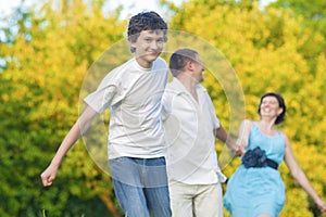 Happy Caucasian Family of Three Having Fun Together and Running in Summer Forest With Joined Hands