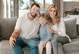 Happy caucasian family of three looking relaxed while sitting and bonding on the sofa together. Adorable little blonde