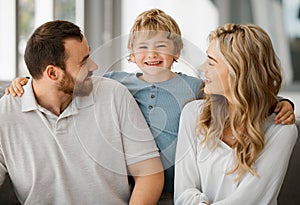 Happy caucasian family of three looking relaxed while sitting and bonding on the sofa together. Adorable little blonde