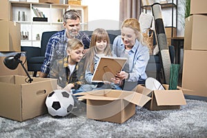 Happy Caucasian family with two kids unpacking boxes at new apartment
