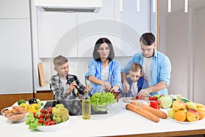 Happy caucasian family with two sons preparing healthy vegetarian breakfast with and vegetables on cozy kitchen.