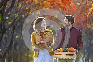 Happy caucasian farmer couple carrying organics homegrown produce harvest with apple, squash and pumpkin while walking along the photo