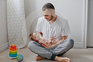 Happy Caucasian father holding newborn baby on laps knees. Man parent embracing rocking child daughter son. Authentic lifestyle