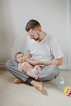 Happy Caucasian father holding newborn baby on laps knees. Man parent embracing rocking child daughter son. Authentic lifestyle