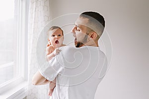 Happy Caucasian father holding newborn baby. Male bearded man parent imitating his yawning child daughter son. Authentic lifestyle