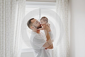 Happy Caucasian father kissing newborn baby. Male man parent holding rocking child daughter son in his hands. Authentic lifestyle