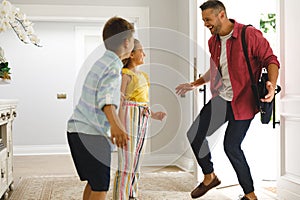 Happy caucasian father returning home with daughter and son smiling and greeting him at front door