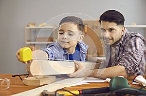 Happy caucasian father and son measuring wood plank with tape at home workshop