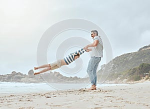 Happy caucasian father swinging and spinning his cute son in circles by the arms at the beach. Playful kid having fun