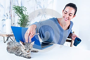 Happy Caucasian female on a desk petting her pet cat lying on the laptop at home