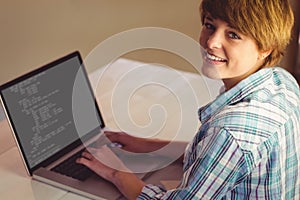 Happy caucasian female programmer sitting at desk, using laptop with coding on screen