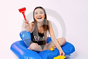 A happy caucasian girl in a black swimsuit sits on an inflatable mattress and recalls her childhood. Plays with sand