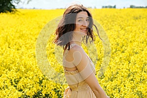 Happy caucasian girl with curly hair in canola field with yellow flowers on sunny summer day, closeup portrait. Young woman