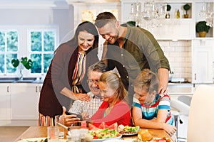 Happy caucasian grandfather and parents with son and daughter looking at smartphone at dinner table