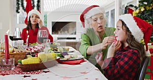 Happy caucasian grandmother wiping her granddaughter mouth at christmas table