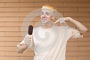 Happy caucasian guy holding an ice cream stick in his hand and pointing and looking his finger at it