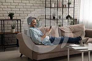 Happy Caucasian man in headphones using smartphone relaxing at home