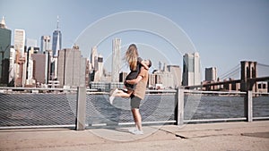 Happy Caucasian man holding his girlfriend in arms smiling at famous Brooklyn Bridge view in New York slow motion.