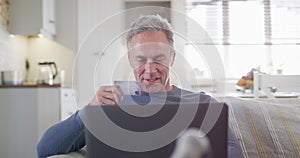 Happy caucasian man sitting on sofa in living room, using laptop and holding credit card