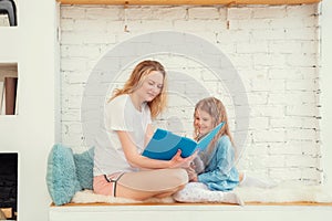 Happy caucasian mom with her daughter reading a book and smiling